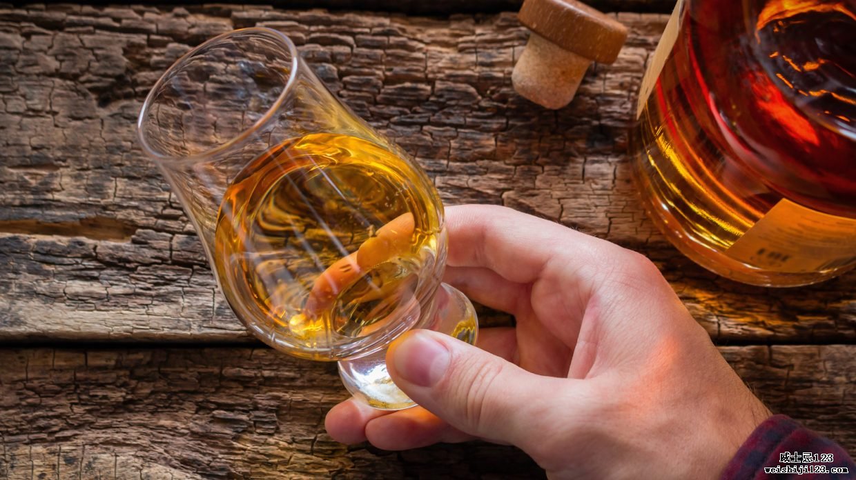 手把威士忌放在玻璃杯里，在木质背景下品尝